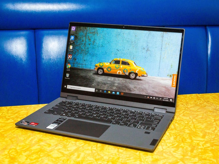 An open Lenovo Chromebook on a yellow tabletop against a blue background.