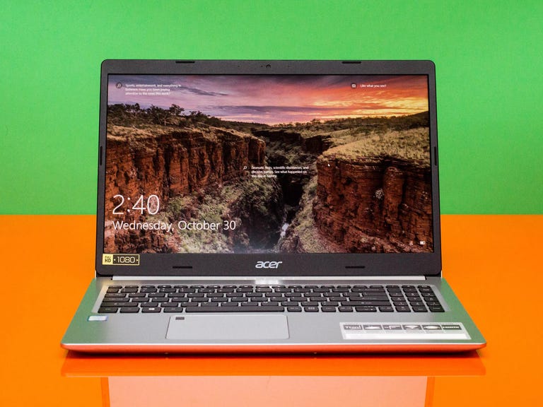 An Acer Aspire 5 laptop on an orange countertop with a green background.