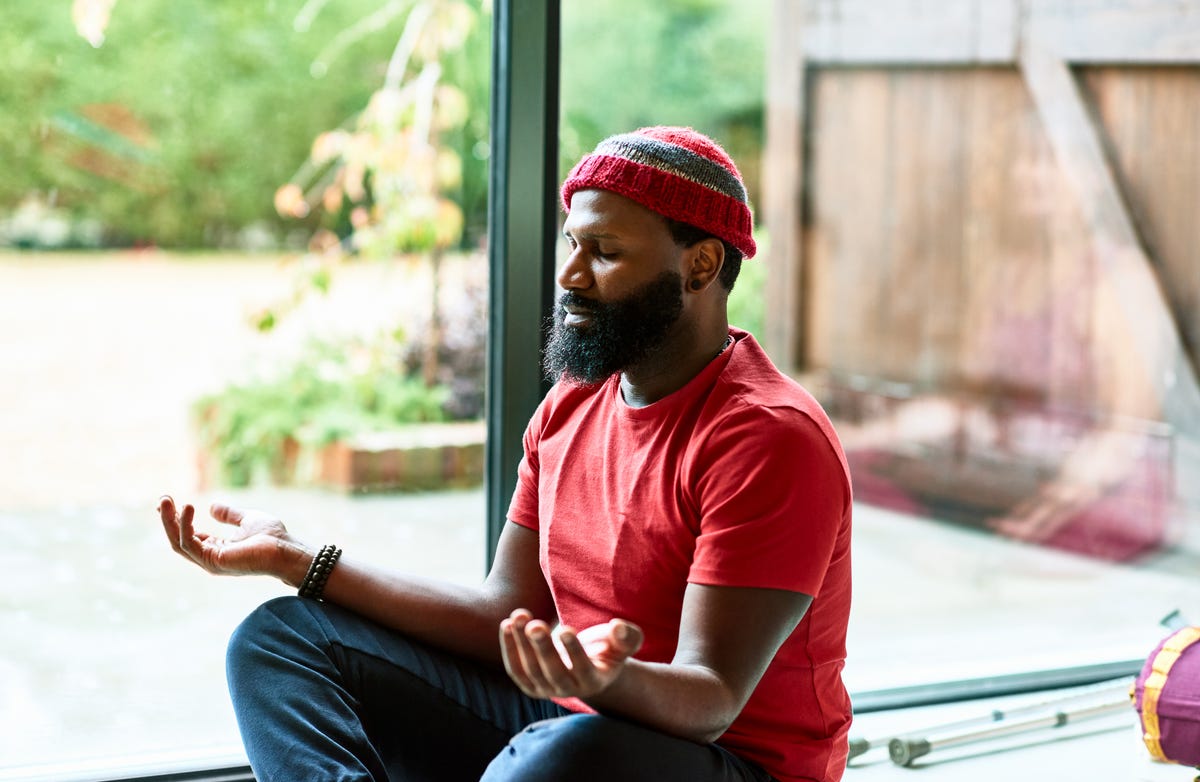 Black man in a red shirt meditates by an open door.