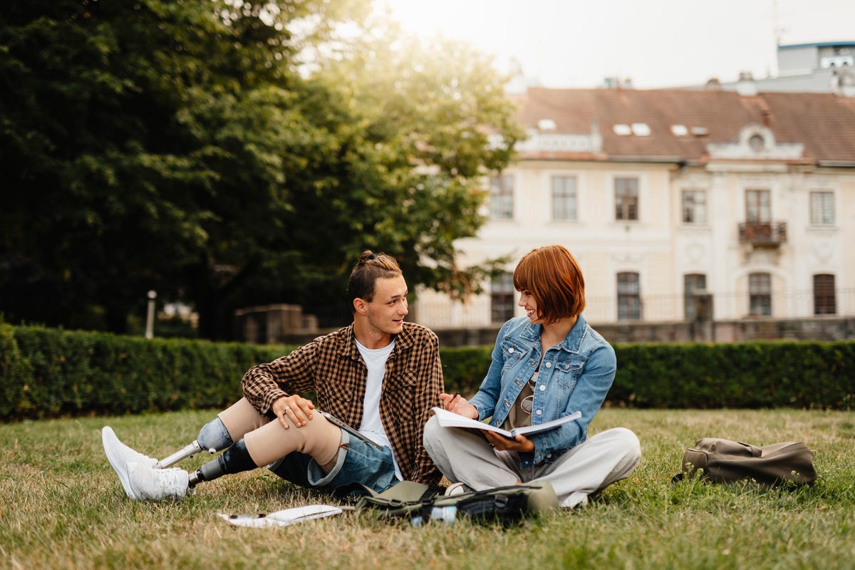 Two friends smiling at each other while studying in a grassy park.