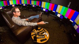 CNET editor David Katzmaier sits on a couch in front of seven TVs showing test patterns